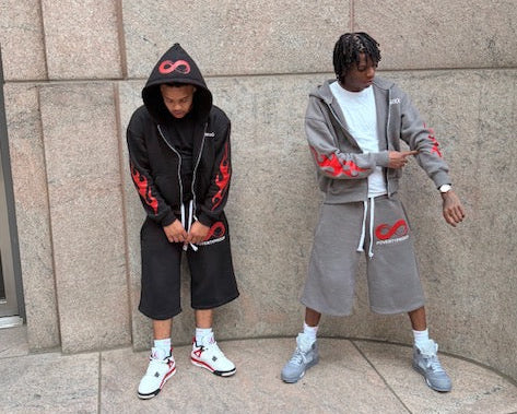 Two individuals wearing matching outfits with red designs against a stone wall.